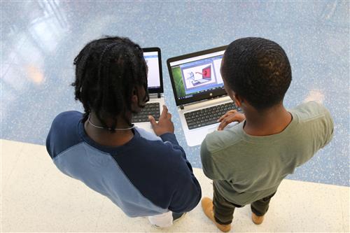 Two students on laptops  in a hallway 